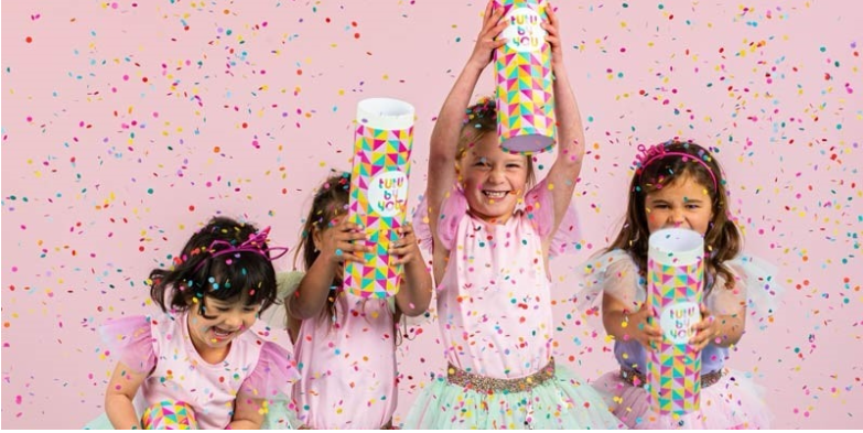 Four young girls dressed in colourful outfits release sparkles from small tubes labelled 'tutu by you'