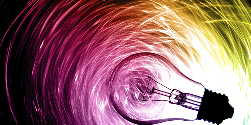 A light bulb lying on its side surrounded by a gradient swirl of green, yellow and pink cables.