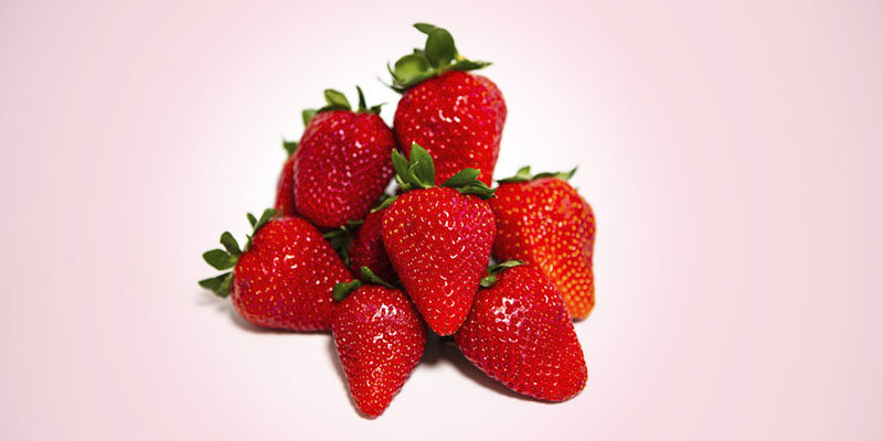 A stack of dark red strawberries on a pink background