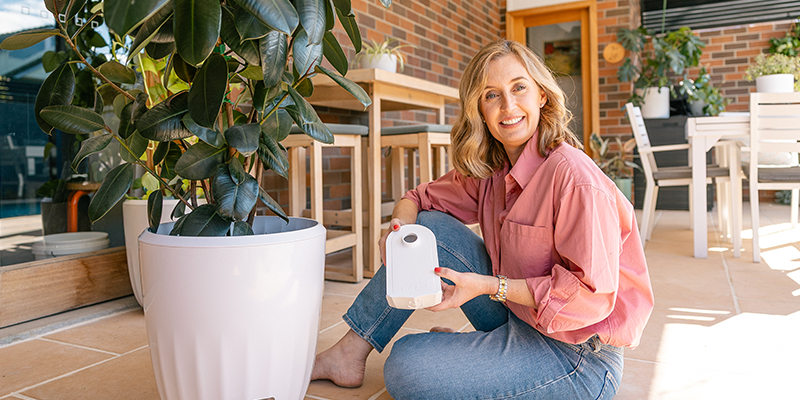 A person sitting indoors next to a white PerkyPod plant pot in a modern living space.