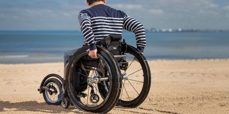 A man in a wheelchair looks across the ocean at the beach