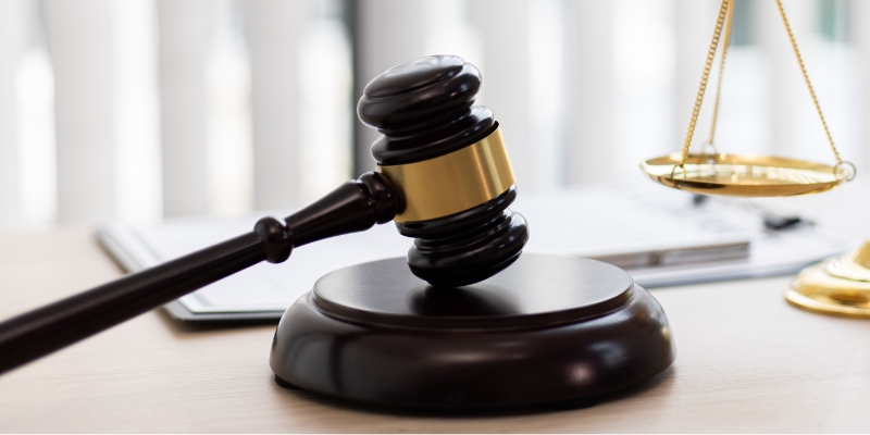 Judge hammer on a desk beside a notepad and the scales of justice