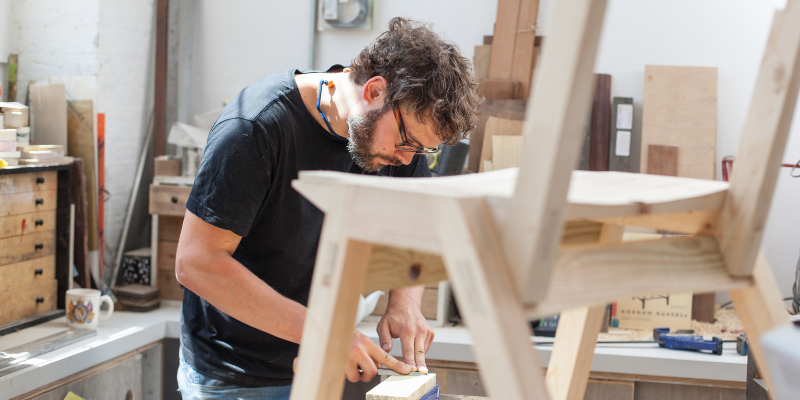 Male carpenter builds chair and draws out sketch