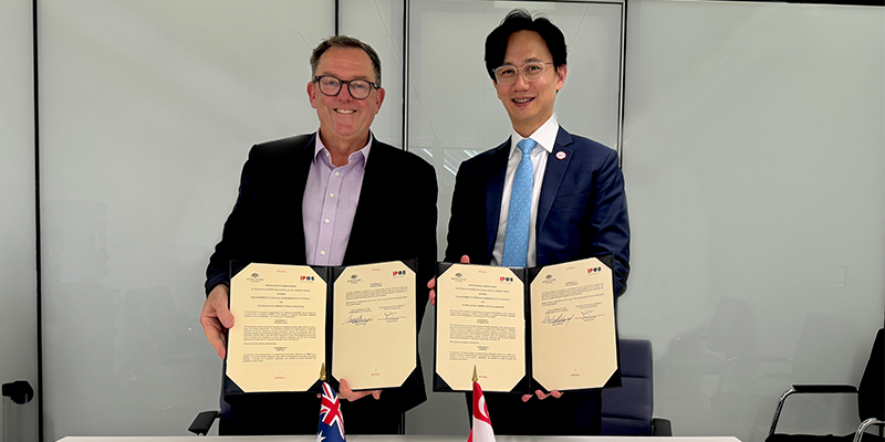 IP Australia Director General Michael Schwager and IP Office of Singapore Chief Executive Tan Kong Hwee stand together in suits holding a signed patent treaty.