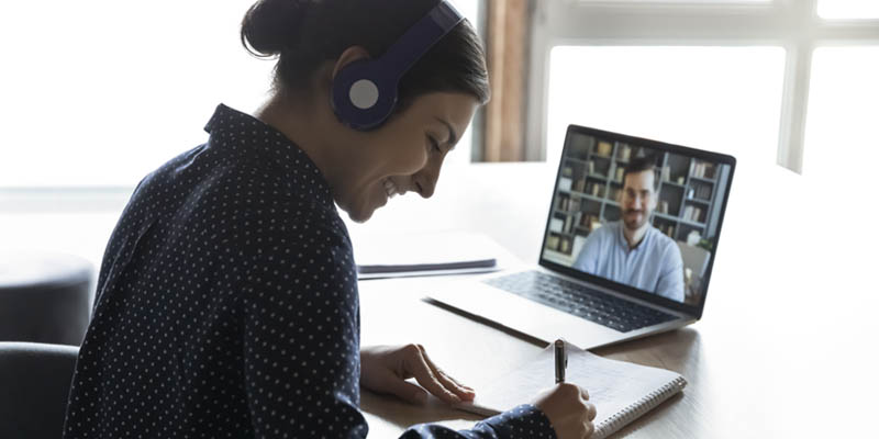 A happy girl wearing headphones. She is watching an educational webinar and writing notes.