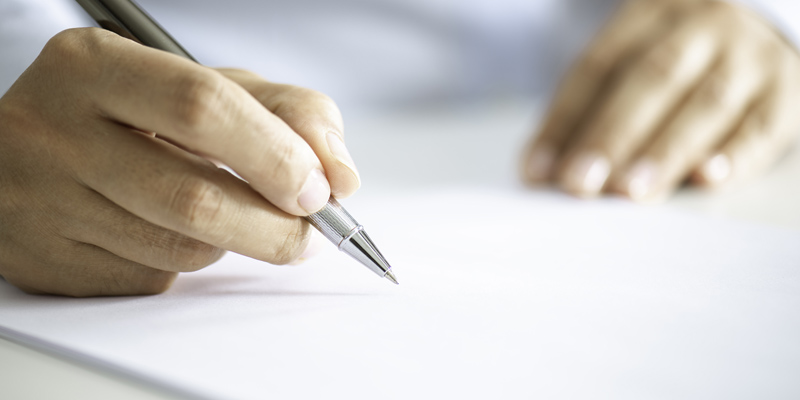 Close-up of a hand holding a pen and writing on a sheet of paper.
