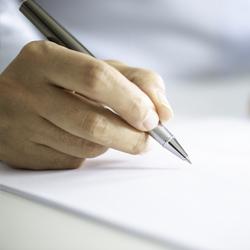 Close-up of a hand holding a pen and writing on a sheet of paper.