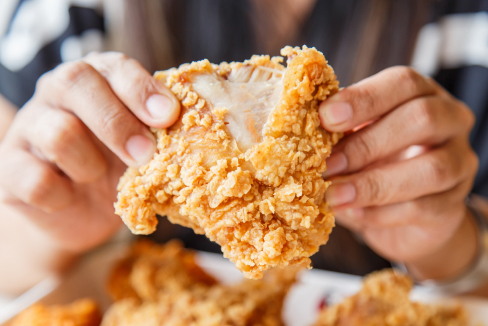 Hands delicately tearing a piece of fried chicken in half.